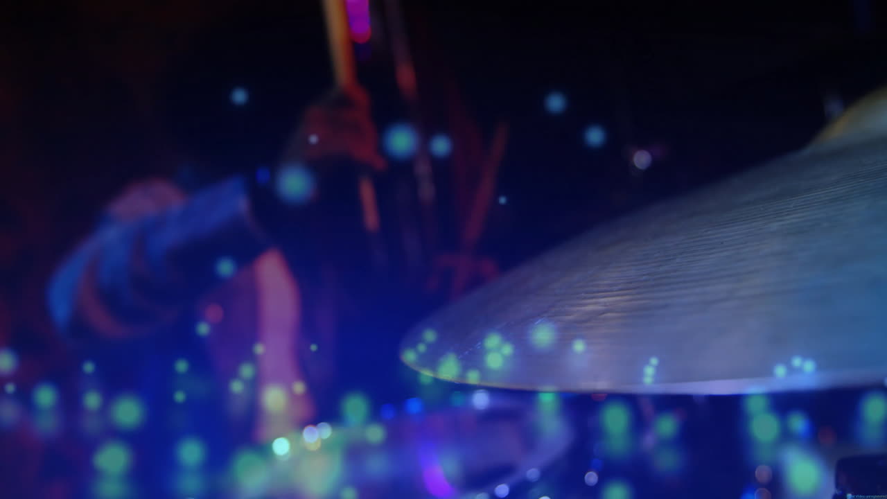 Batterista uomo che agita le bacchette su un palco di musica dal vivo, con bokeh colorati animati che fluttuano