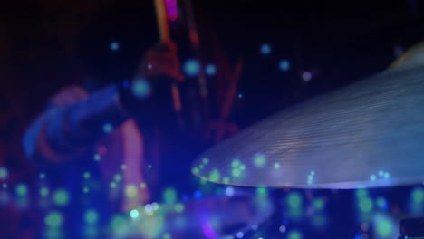 male drummer swinging drumsticks on live music stage, with animated colored bokeh floating