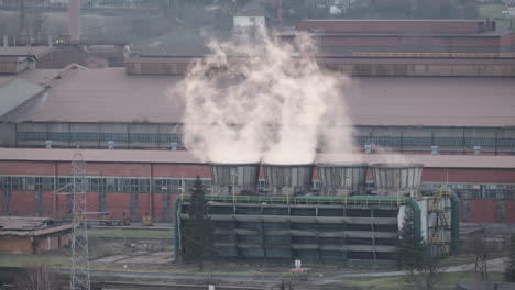 billowing steam from cooling towers at an industrial facility with large factory buildings, highlighting industrial operations