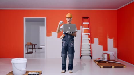 full body of asian man painter wearing safety helmet looking at the laptop then screaming goal celebrating while standing with painting wall in room