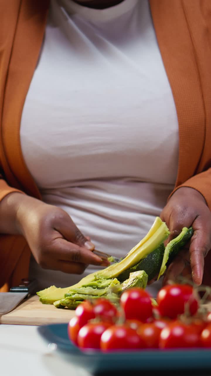 Video verticale: donna che affetta avocado per toast, primo piano, video di cucina, donna al bancone.