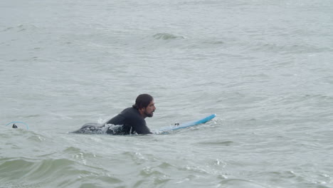 sportive man in wetsuit with artificial leg lying on surfboard and swimming in the ocean 6