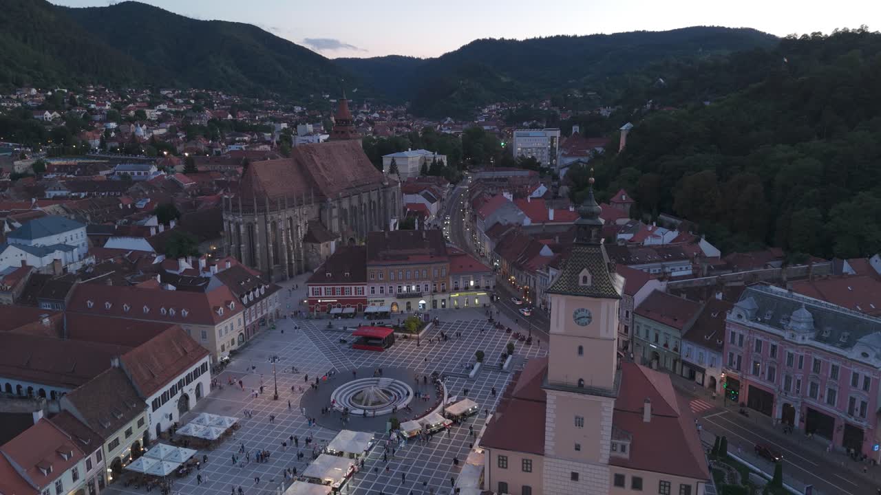 Dron cofa się nad Rynek Ratuszowy (Piața Sfatului) nocą, ukazując oświetlony Ratusz w Braszowie, Rumunia