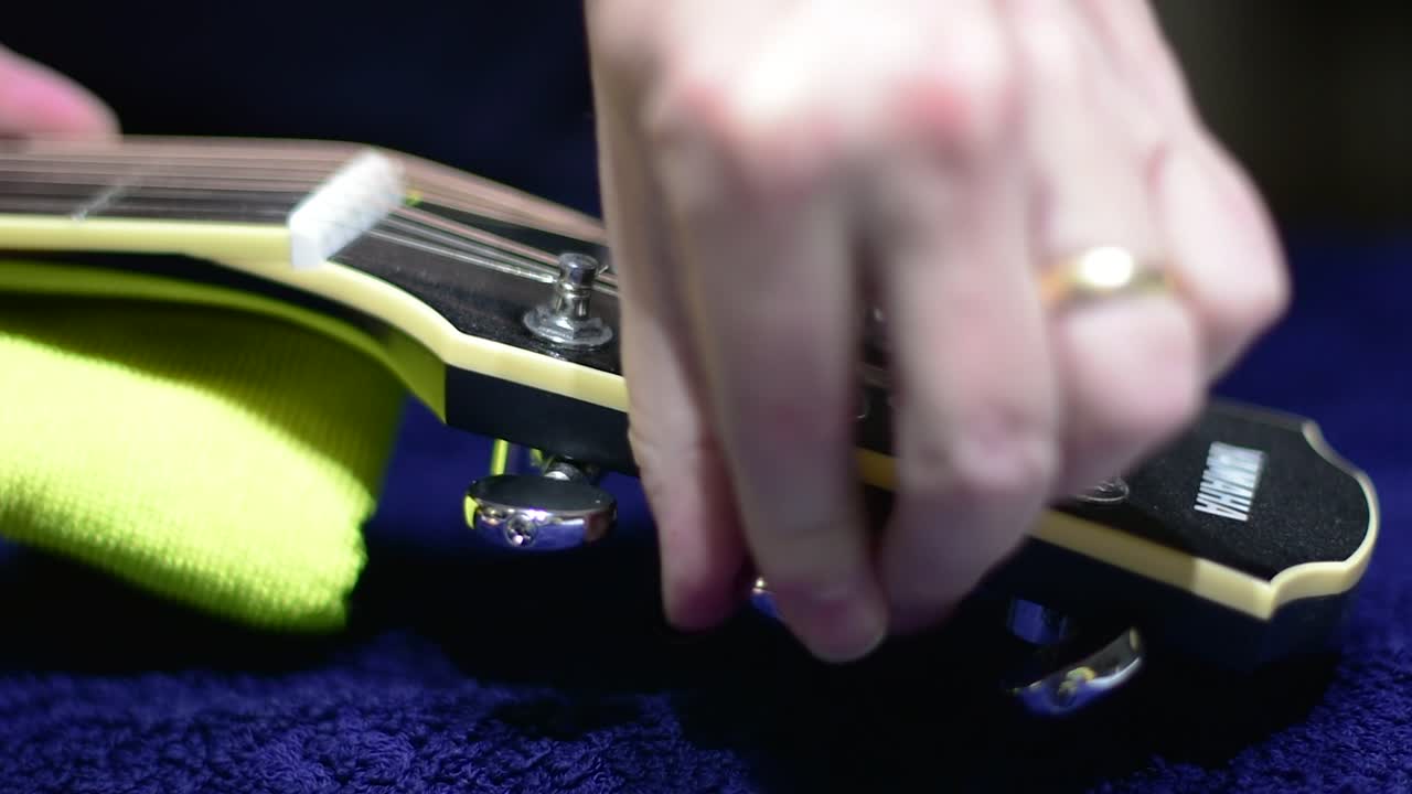 Restringing and cleaning a beautiful black single cutaway accoustic guitar - close up of loosening the strings at the headstock