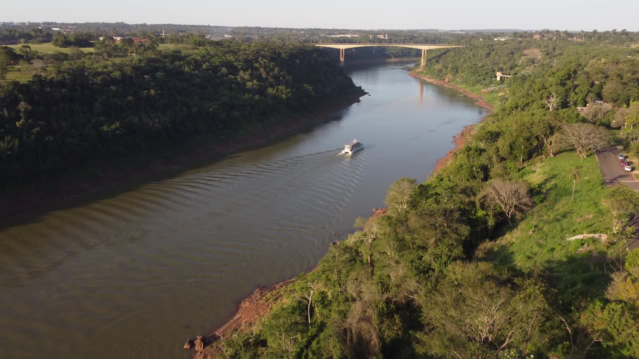 toma panorámica con drones de un barco turístico navegando en la frontera del río iguazú entre argentina y brasil durante la puesta de sol dorada