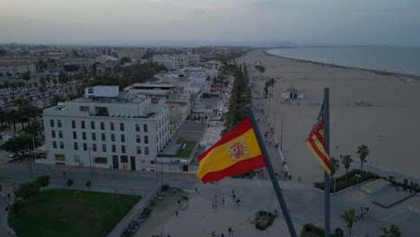 Aerial-view-of-Spanish-flags-at-beach-promenade-in-Valencia-during-summer-twilight,-evening