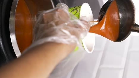 disparo vertical de un cocinero vertiendo sopa de tomate en una taza de cartón