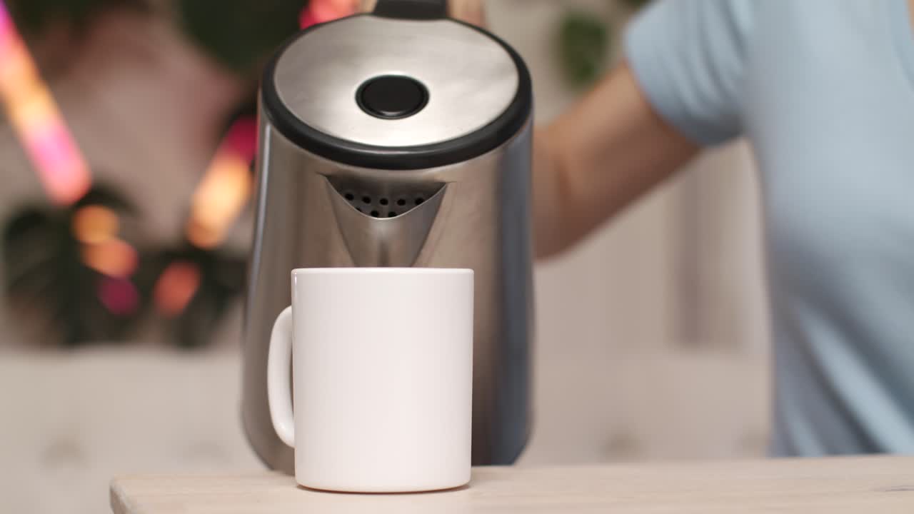 여자 는 전기 케이틀 에서 물 을 잔 에 부어 넣고 있다