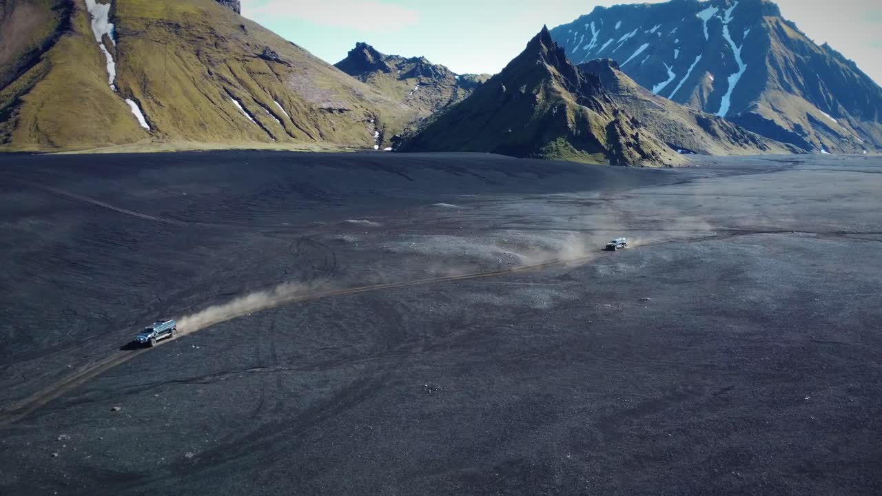 dos vehículos haciendo todoterreno en un amplio desierto frente al paisaje de altas montañas, islandia
