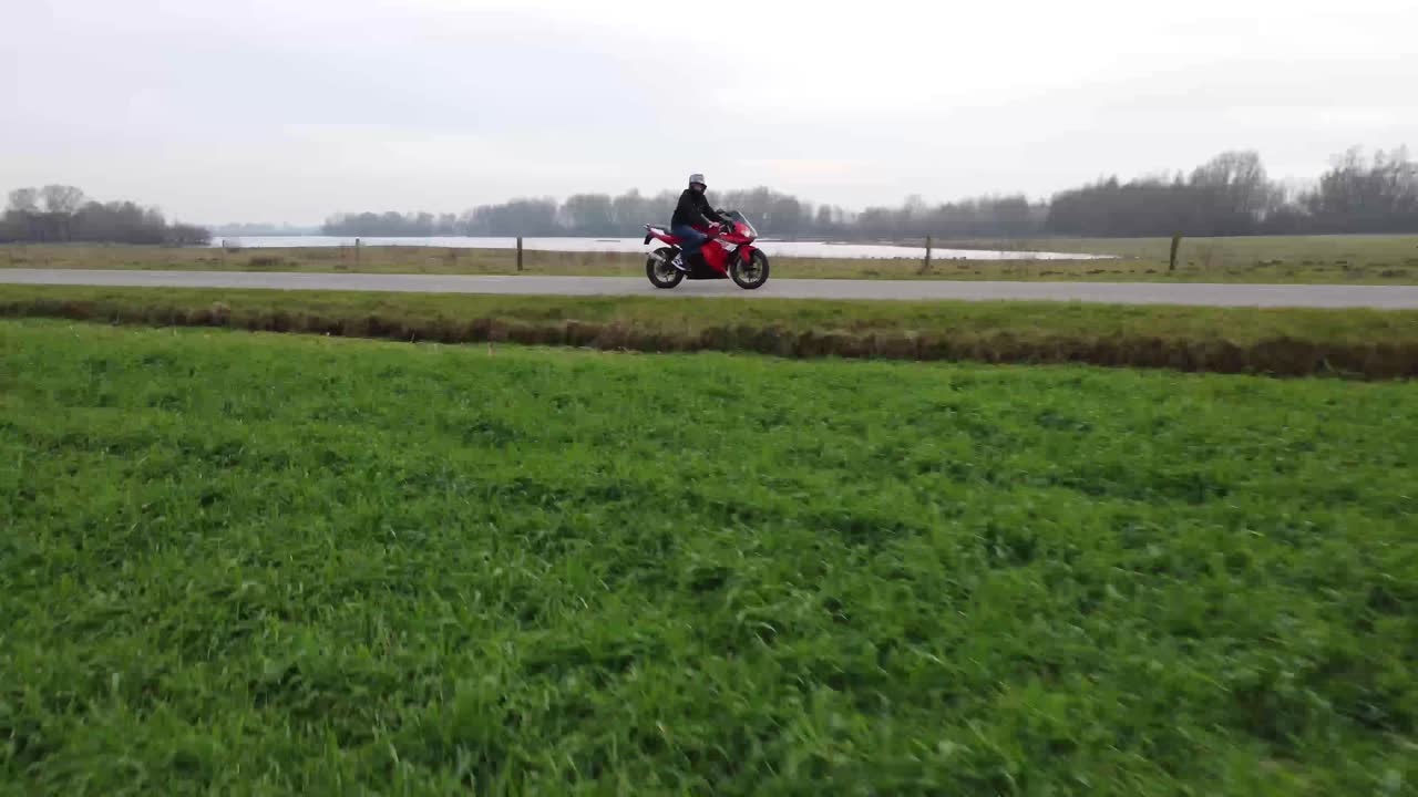 잔디밭 옆 도로를 운전하는 오토바이 운전자의 빠르게 움직이는 드론 샷