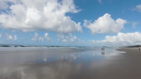 Couple-strolling-along-Melbourne-beach-with-fluffy-white-clouds-and-blue-skies