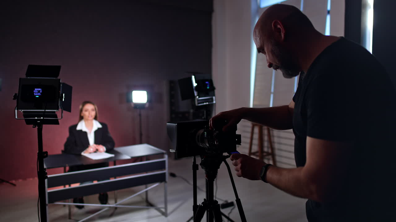 Male photographer recording a video with a woman sitting at desk. Cameraman looks at camera display and laughs.