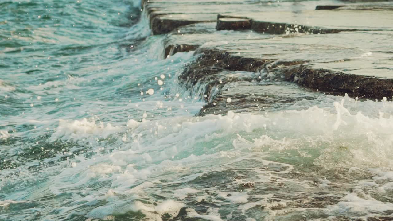 Onde del mare lambiscono le rocce vicino alla riva durante il giorno. Slow motion.