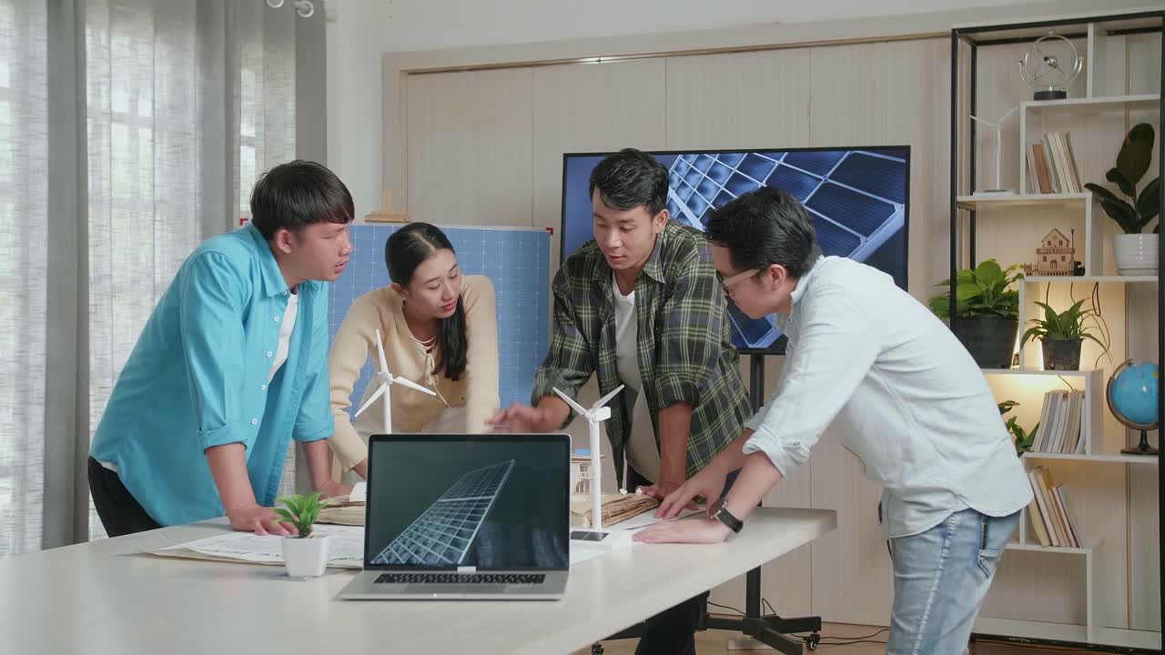 테이블 위의 노트북은 태양전지를 보여주고 있으며, 아시아 엔지니어 그룹은 사무실에서 태양 전지판을 가진 작은 집 모델에 대해 논의하고 있습니다.