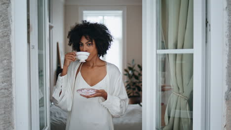 Entspanntes-Modell-Trinkt-Kaffeetasse-Aus-Der-Nähe-Vom-Fenster.-Frau-Mit-Dunkler-Haut-Schaut-Auf-Die-Straße