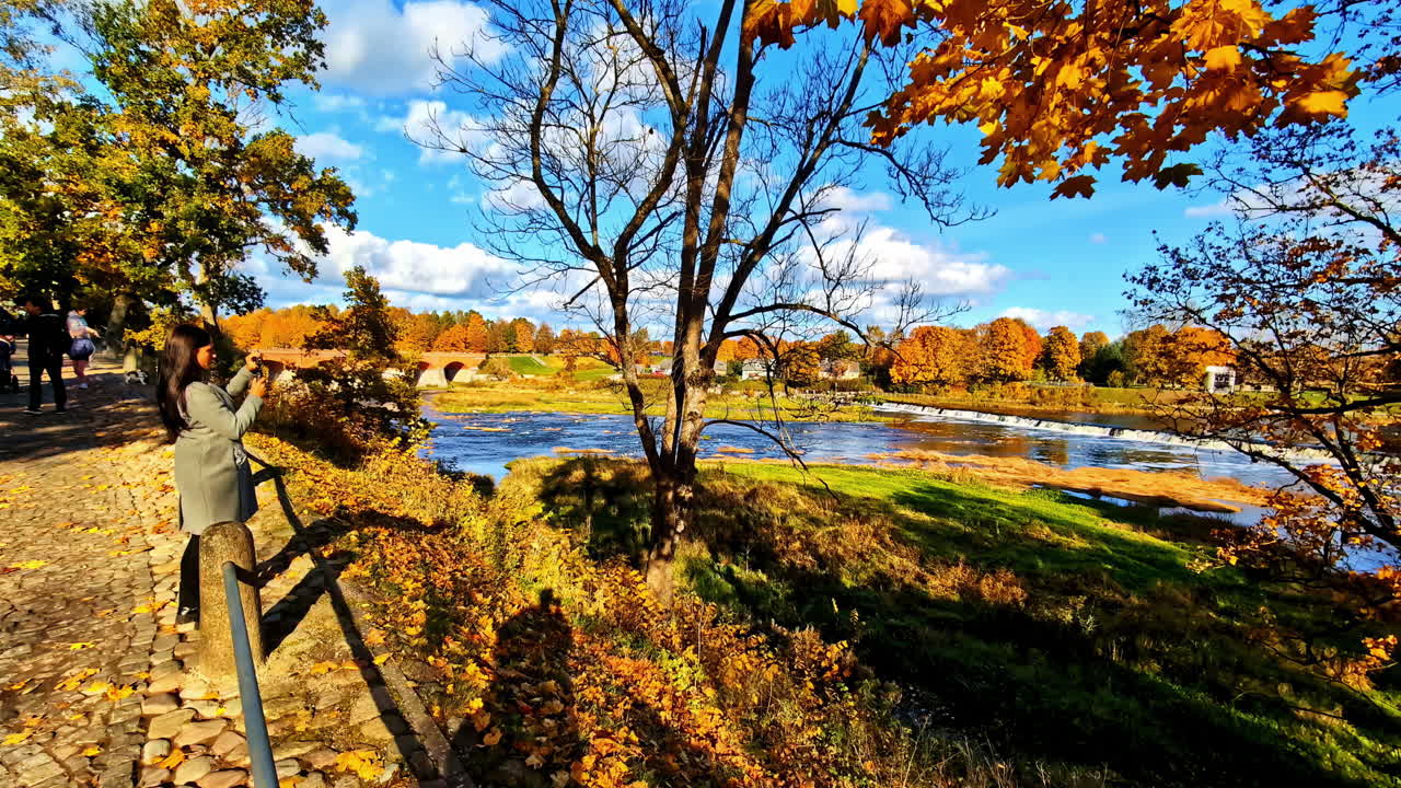 A woman takes pictures of autumn-colored trees reflecting on a calm lake in fall season