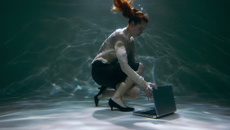 Working on the go. Beautiful young software expert woman dives underwater to pick laptop up, swims away slow motion.