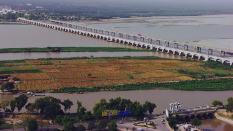 Aerial-view-of-twins-bridges-over-the-river-and-city-with-electric-towers,-big-canal-starting-from-the-river-going-between-the-city,-Rural-and-urban-areas-gathered-Khyberpakhtunkhwa,-Pakistan