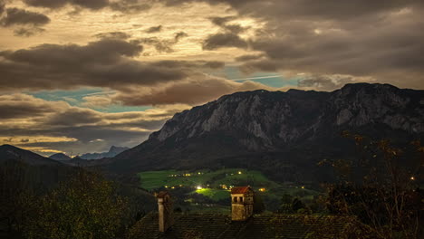 Abendwolken-Tanzen-Im-Zeitraffer-über-Der-Reiteralm,-Österreich,-Mit-Einem-Leuchtenden-Dorf-Darunter