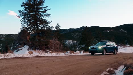 impresionante toma de seguimiento de un todoterreno azul conduciendo a lo largo de un camino de montaña de tierra nevada durante la puesta de sol