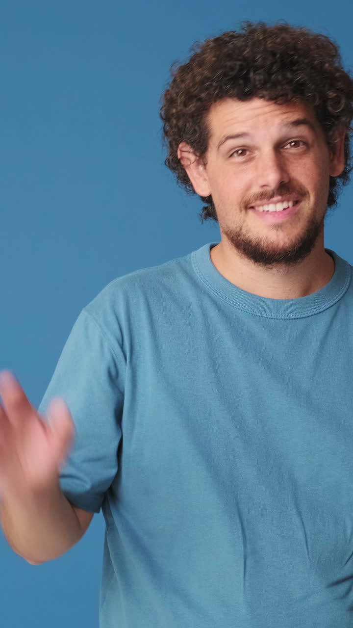 Giovane uomo che saluta e sorride su sfondo blu
