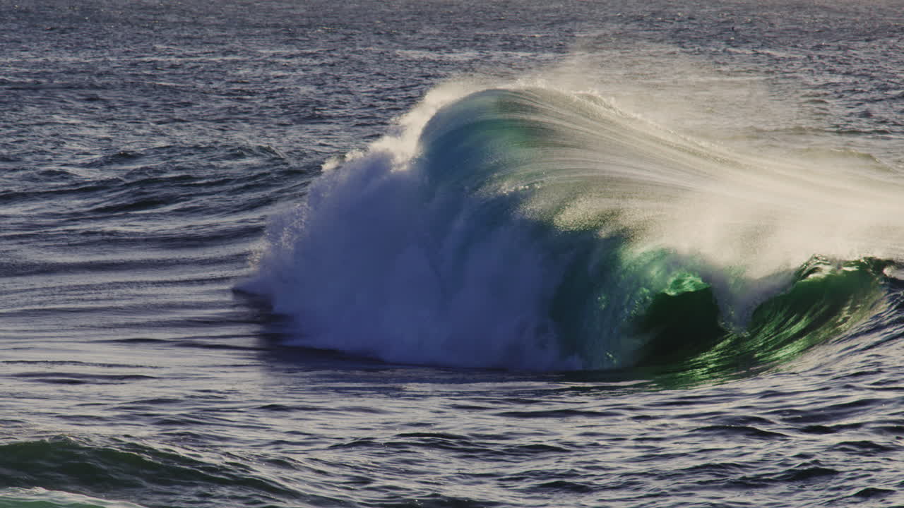 Slow motion backdrop background of ocean wave crashing, backlit green with ocean spray erupting