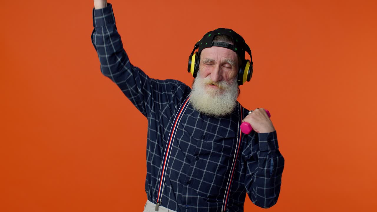 Äldre skäggig man lyssnar på musik via hörlurar, tränar, lyfter rosa hantlar, hälsa.