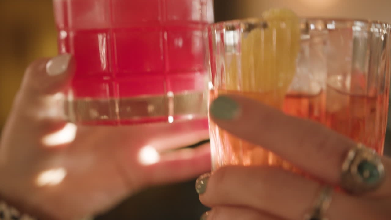 Slow motion: Mani femminili che brindano con bicchieri da cocktail in un bar illuminato dal sole.