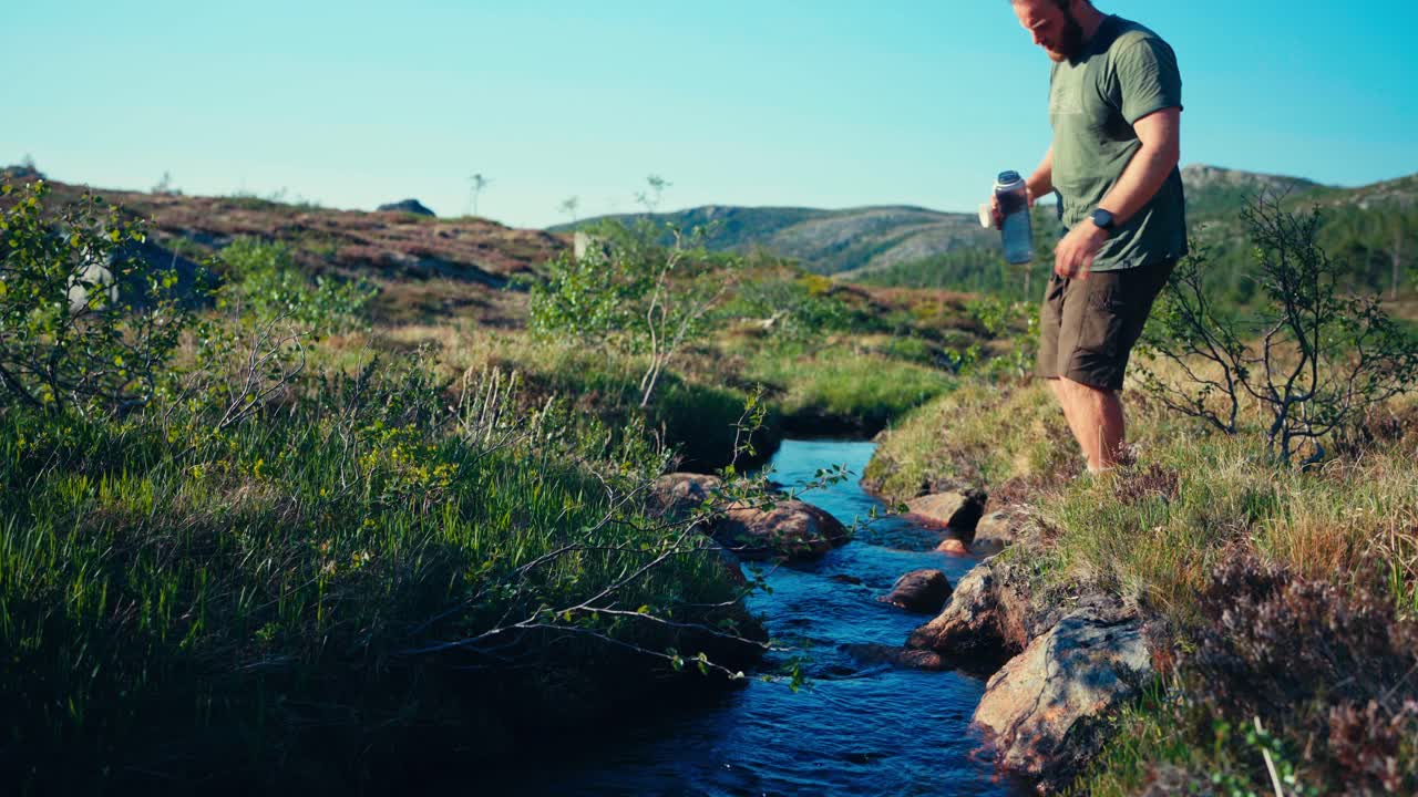 un excursionista masculino bebiendo agua del arroyo en indre fosen, noruega - toma amplia