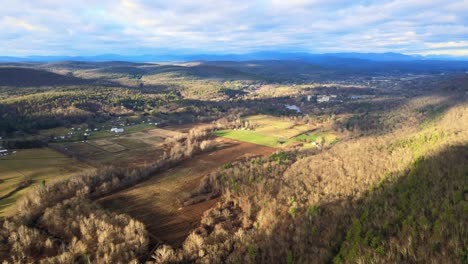 A-drone-high-over-a-mountain-valley-during-sunset-panning-sideways-with-mountains-in-the-distance-during-autumn-in-the-northern-Appalachians-with-farmland-below