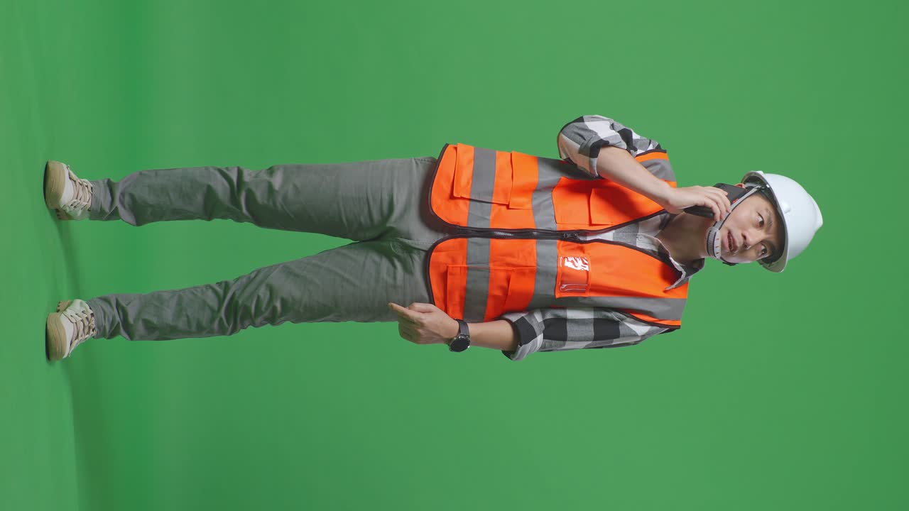 Full Body Of Asian Male Engineer With Safety Helmet Talking On Smartphone While Standing In The Green Screen Background Studio
