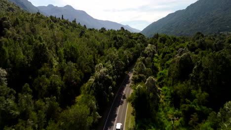 car travels beside petrohue river as drone captures lush chilean forest and curving road, aerial rearview tracking