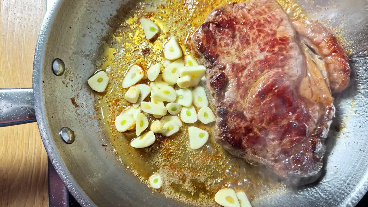 Una mano mette l'aglio nella padella mentre la bistecca cuoce - Primo piano