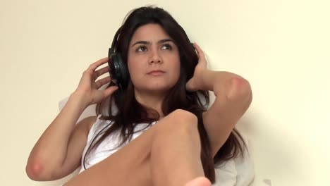 mujer pensativa escuchando música acostada en la cama