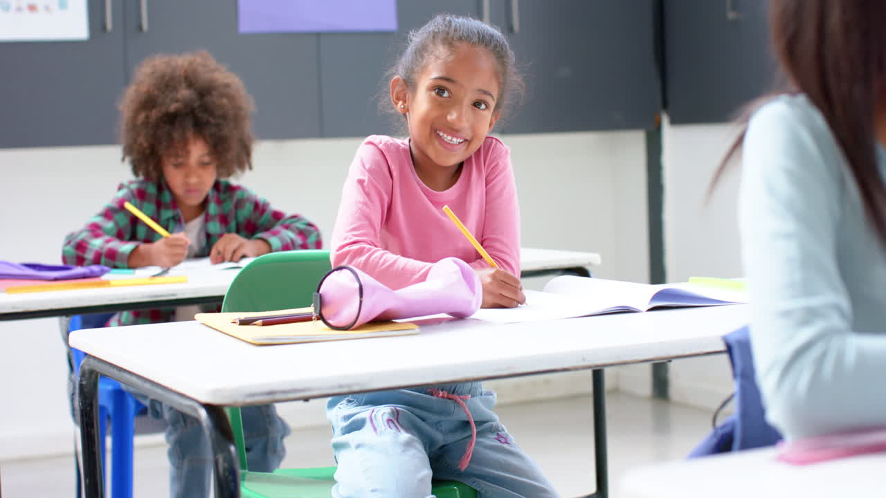 In school, smiling girl writing in notebook at classroom desk, enjoying learning