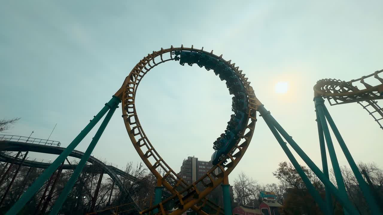 Handheld from an inverted curve, high speed roller coaster going around on the rails, sunny day at an amusement park