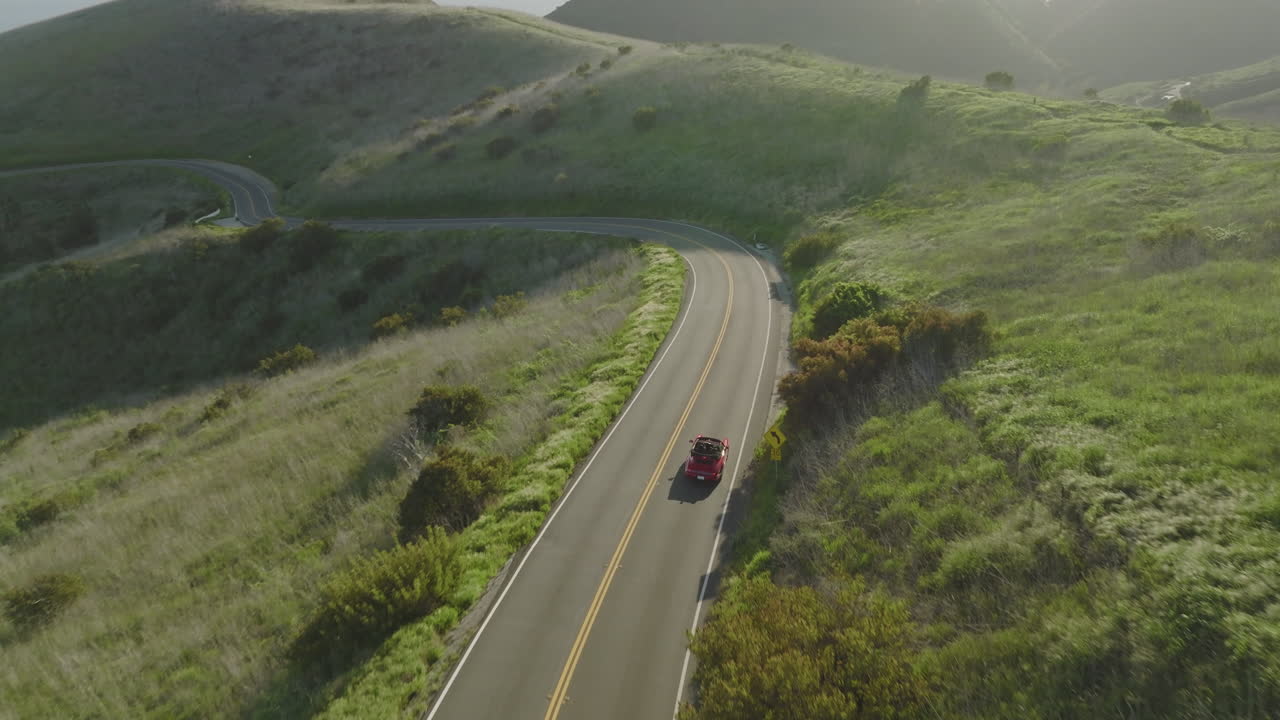 Aerial drone shot follows a red Porsche 1993 Carrera S cruising through the mountains of Malibu
