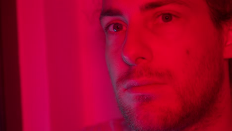 side profile of man in red lighting, thoughtful expression as he raises head up and nods looking forward, shadows create a dramatic effect