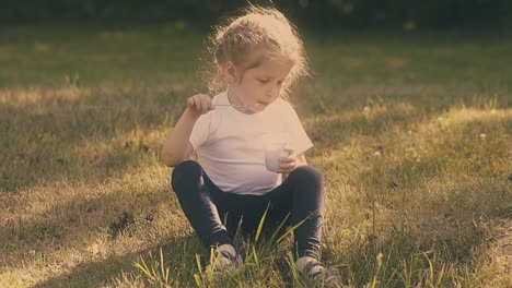 young lady eats yogurt with metal spoon sitting on meadow