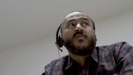 casual ethnic minority uk asian male talking on headset in white office room