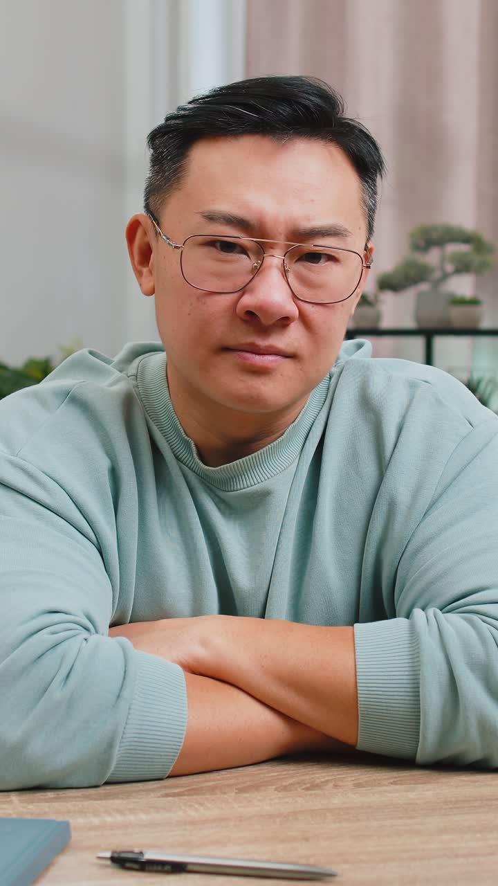 Upset chinese man showing thumbs down dislike bad work disapproval dissatisfied feedback at home