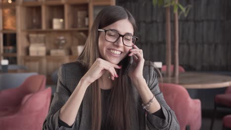 A-happy-and-charming-brunette-holds-a-pleasant-conversation-via-phone,-She-is-very-amused-by-the-stories-of-her-interlocutor