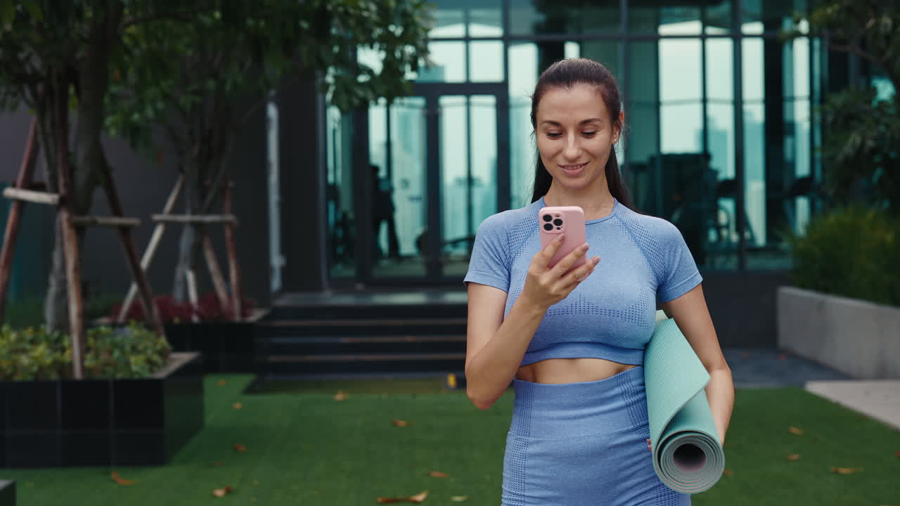 Woman using phone outdoors while holding yoga mat