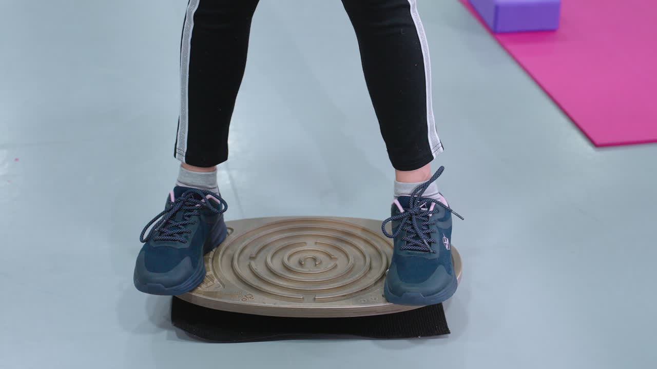 피트니스 세션 중에 런스 보드 위에 서 있는 스니커와 조을 입은 사람의 낮은 각도 관측, 개인은 안정성과 조정에 초점을 맞추고 있습니다.