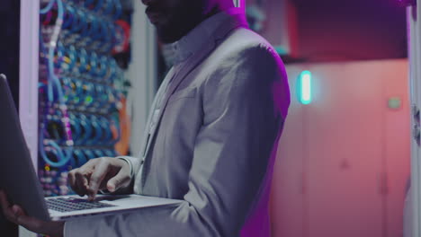 black it engineer working on laptop in server room