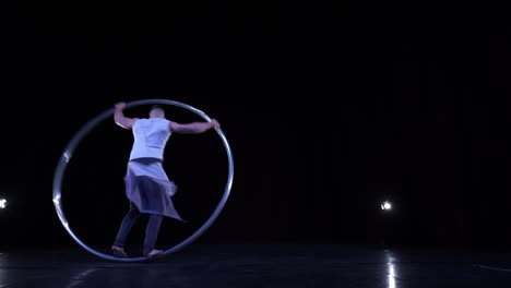 cyr wheel performer shows tricks on a black stage with smoke