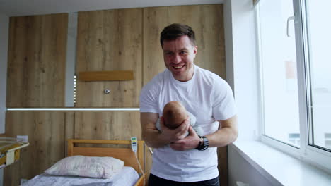 man is overwhelmed with happiness holding his newborn baby. smiling father waving his infant in the hospital ward.
