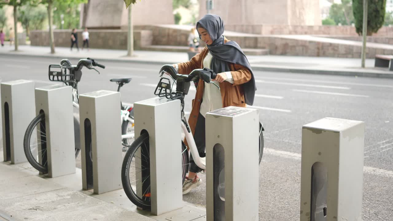 Woman in hijab renting a public bicycle from a bike-sharing station in the city
