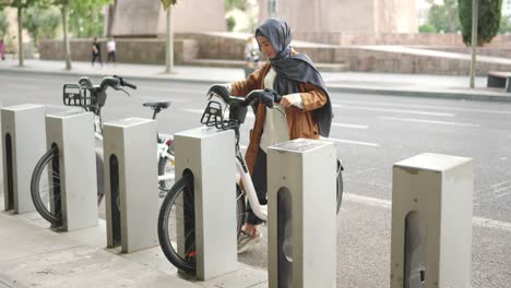 woman in hijab renting a public bicycle from a bike-sharing station in the city