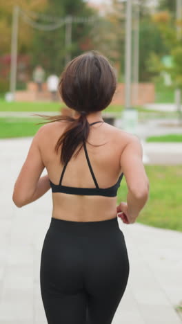 Back view of athletic woman running in park with decorative benches and poles in background, ideal for fitness, outdoor workouts, and active lifestyle content in green urban park setting